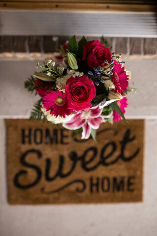 Draufsicht auf einen frischen Blumenstrauß an der Stützmauer neben der Fußmatte am Eingang, lizenzfreies Stockfoto