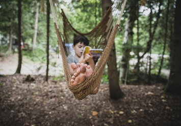 Junge liest in voller Länge ein Buch und entspannt sich in einer Hängematte im Wald - CAVF62152