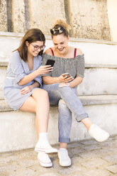 Full length of smiling female tourists using phone while sitting on steps - CAVF62170