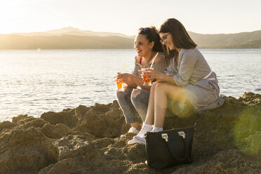 In voller Länge der weiblichen Freunde mit Getränk, während auf Felsen am Strand sitzen - CAVF62176