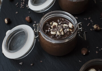Nahaufnahme von Schokoladensauce im Glas mit Nüssen auf Schiefer - CAVF62193