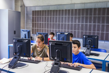 Hochformatige Ansicht eines Lehrers mit Schülern, die Computer im Klassenzimmer benutzen - CAVF62198