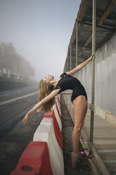 Seitenansicht einer Ballerina in einem schwarzen Trikot, die sich auf einem Bürgersteig in der Stadt streckt - CAVF62208