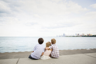 Rückansicht von Geschwistern, die auf der Strandpromenade sitzen, gegen den Himmel - CAVF62223
