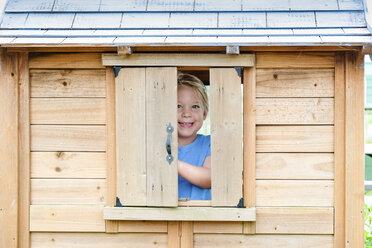 Portrait of smiling girl standing at window in wooden playhouse - CAVF62226