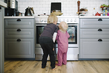 Rückansicht von Geschwistern mit Blick auf den Ofen in der Küche - CAVF62227