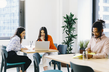 Businessman reading documents while female colleagues discussing over laptop computer in office - CAVF62251