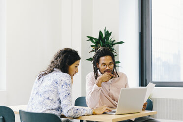 Businesswoman discussing data over laptop computer with businessman in office - CAVF62254