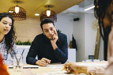 Businessman explaining documents to colleagues at desk in creative office - CAVF62261