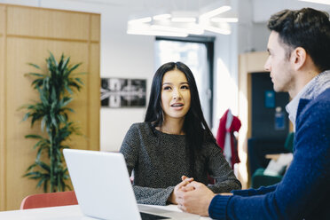 Businesswoman discussing over laptop computer with male colleague in cafeteria at office - CAVF62278