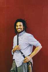 Porträt eines glücklichen Geschäftsmannes mit Umhängetasche vor einer roten Wand in einem kreativen Büro - CAVF62282