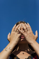 Low angle view of woman covering face with hands while standing against clear blue sky during sunny day - CAVF62287