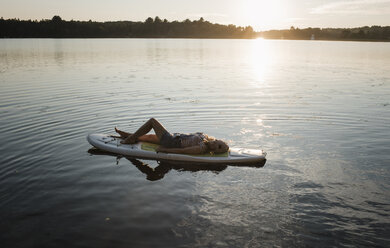 Hohe Winkel Ansicht der Frau auf Paddleboard im See gegen den Himmel während des Sonnenuntergangs liegen - CAVF62294