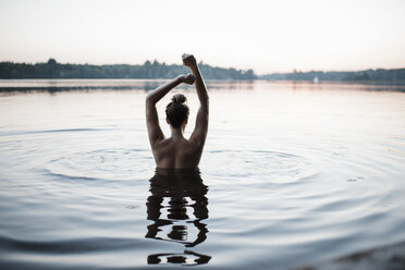 Rear view of topless woman with arms raised swimming in lake against clear sky during sunset - CAVF62298