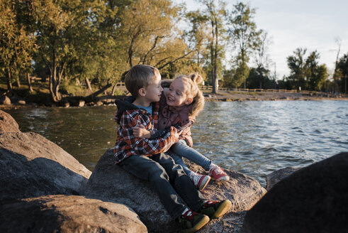 Glückliche Geschwister sitzen bei Sonnenuntergang auf einem Felsen am Lake Simcoe - CAVF62311
