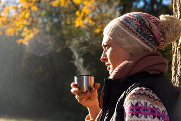 Woman having warm drink in autumnal forest - CUF49268