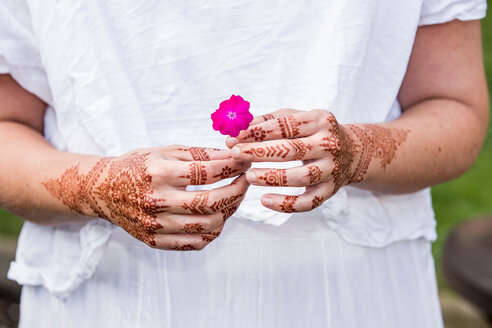 Frau in weißem Kleid mit Henna-Tätowierung auf den Händen hält Blume - CUF49360