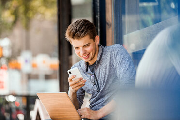 Junger Mann mit Smartphone und Laptop in einem Cafe - CUF49367
