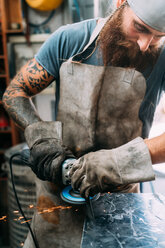 Axe maker using steel grinder in workshop - CUF49383