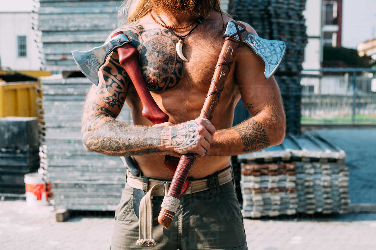 Tattooed man showing off handcrafted axes stock photo