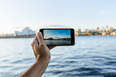 Australia, New South Wales, Sydney, close-up hand of man taking a picture with mobile phone to Sydney - KIJF02356