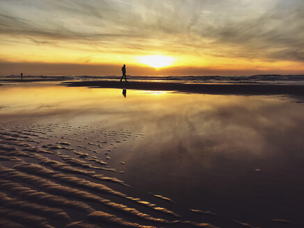 Belgium, Flanders, North Sea Coast, man walking along tide pool watching sunset and ocean waves, listening to the ocean sounds - GWF05906