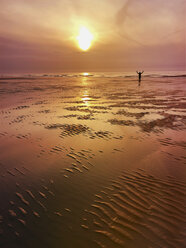 Belgium, Flanders, North Sea Coast, man relaxing, doing excercise and enjoying freedom while watching sunset and ocean waves, listening to ocean sounds - GWF05907