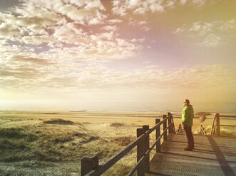 Belgium, Flanders, North Sea, Coast, sunset light, man standing on boardwalk in sand dunes, relaxing, watching ocean and listening to ocean sounds - GWF05914