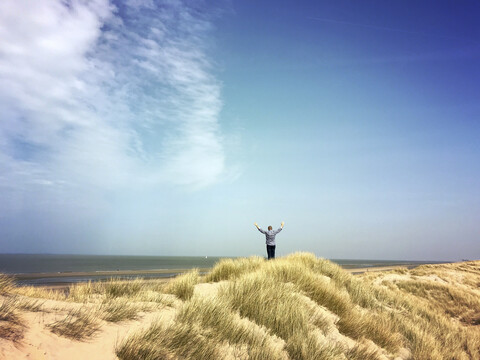 Belgien, Flandern, Nordsee, Küste, Mann entspannt sich in den Sanddünen, treibt Sport und beobachtet das Meer, lauscht den Meeresgeräuschen in der warmen Frühlingssonne, lizenzfreies Stockfoto