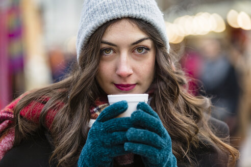 Porträt einer schönen jungen Frau mit einem heißen Getränk auf dem Weihnachtsmarkt - MGIF00307