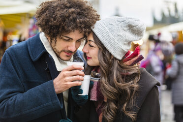 Glückliches, zärtliches junges Paar mit heißen Getränken auf dem Weihnachtsmarkt - MGIF00308