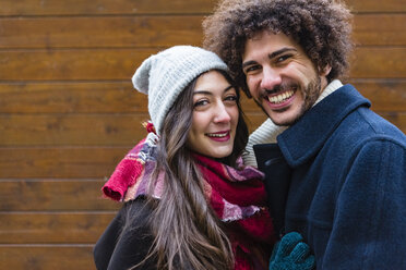 Portrait of happy young couple in winterwear in front of wooden wall - MGIF00315