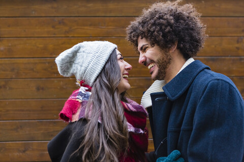 Glückliches junges Paar in Winterkleidung vor einer Holzwand, lizenzfreies Stockfoto