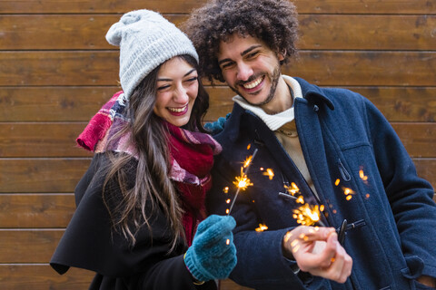 Glückliches junges Paar in Winterkleidung mit Wunderkerzen vor einer Holzwand, lizenzfreies Stockfoto