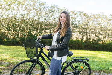 Porträt einer lächelnden jungen Frau mit Fahrrad im Park - KIJF02361