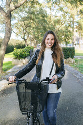 Portrait of smiling young woman with bicycle in park - KIJF02366