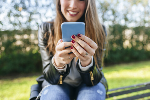 Nahaufnahme einer jungen Frau, die auf einer Bank im Park sitzt und ein Handy benutzt, lizenzfreies Stockfoto