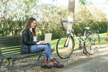 Young woman sitting on a bench in park using laptop - KIJF02371
