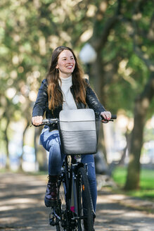 Lächelnde junge Frau beim Fahrradfahren im Park - KIJF02377