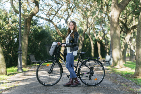 Porträt einer lächelnden jungen Frau mit Fahrrad im Park - KIJF02378