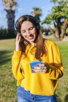 Glückliche junge Frau mit Handy, die mit Kopfhörern Musik hört - KIJF02387