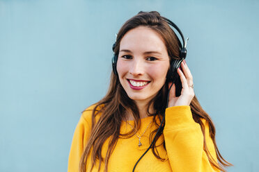 Porträt einer lächelnden jungen Frau, die mit Kopfhörern Musik hört - KIJF02408