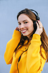 Porträt einer lächelnden jungen Frau, die mit Kopfhörern Musik hört - KIJF02409