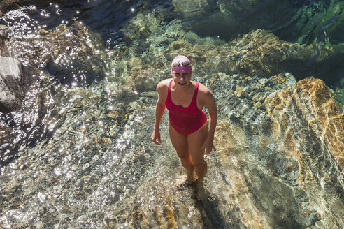 Switzerland, Ticino, Verzasca Valley, portrait of happy woman in swimsuit standing in Verszasca river - GWF05956
