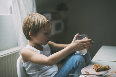 Kleiner Junge mit blauem Nagellack sitzt am Frühstückstisch mit einem Glas Milch - KMKF00773