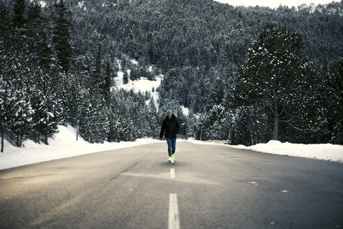 Junger Mann geht auf einer verschneiten Straße mit Bäumen im Hintergrund - ACPF00486