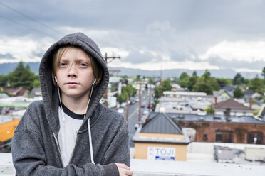 Portrait of boy listening music while standing by retaining wall against cityscape - CAVF62324