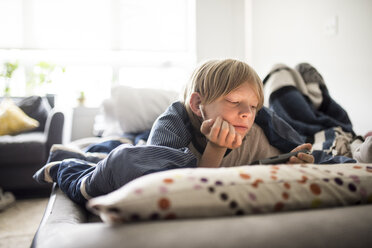 Junge benutzt Mobiltelefon, während er zu Hause auf dem Bett liegt - CAVF62325