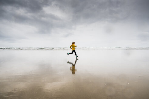 Side view of boy running at beach against cloudy sky - CAVF62328