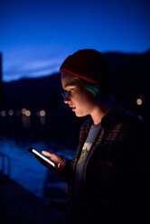 Teenager-Mädchen, das ein Mobiltelefon benutzt, während es gegen den blauen Himmel im Olympic National Park bei Nacht steht - CAVF62329